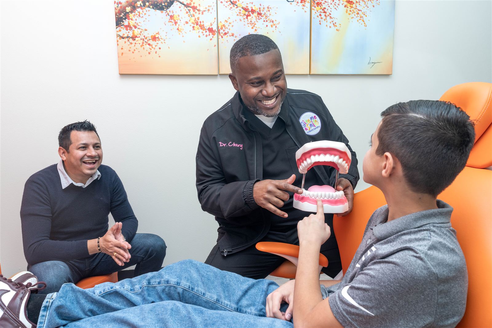 Dr. Chery showing a young patient how teeth work using a large dental model while dad looks on